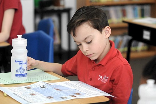 Fourth-grader Andrew VonEschen takes a first look at the Living Water calendar April 2. Each student was given a calendar and a water bottle in which to collect coins. Below, teacher Amy Hohenecker put together a bulletin board in her classroom to introduce her students to the program. Dianne Towalski / The Catholic Spirit