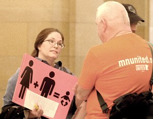 Lizz Paulson talks to a supporter of same-sex marriage while holding a sign protesting the bill to change the definition of marriage. (Dianne Towalski/The Catholic Spirit)