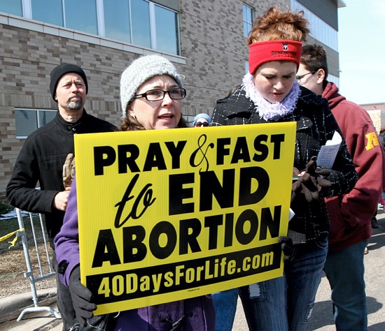 Desiree Schlangen, center, of St. Patrick in Oak Grove carries a sign as she joins the prayer service. Next to her at right is Amy Rhein, also of St. Patrick. At far left and behind Schlangen is her husband Mark. (Dave Hrbacek/The Catholic Spirit)
