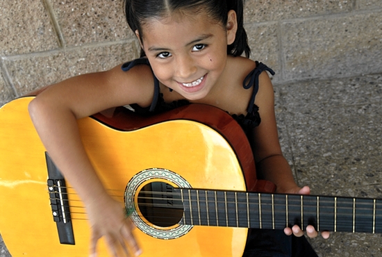 A young girl from the Nuestros Pequeños Hermanos home in El Salvador plays guitar in music class. Photo courtesy NPH USA