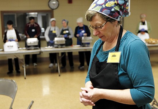 Pat Haas joins in prayer with other volunteers and guests before the meal is served. Haas pours gravy as part of meal for a guest. Dave Hrbacek/The Catholic Spirit 