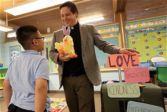 Father Aaron Meszaros uses props including a stuffed chicken and a suitcase covered with placards to teach important spiritual lessons to second-grader Travis Nguyen and other students at St. Alphonsus School in Brooklyn Center. Dave Hrbacek/The Catholic Spirit