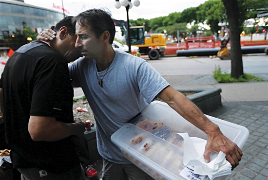 Chris Engelmann of St. Mark and Nativity of Our Lord in St. Paul hugs a homeless man June 15 in downtown St. Paul across the street from the Dorothy Day Center. He is carrying doughnuts donated from a local bakery to offer to those he meets. Some call him the Doughnut Man. Dave Hrbacek/The Catholic Spirit