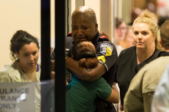 A Dallas police officer is comforted July 7 at Baylor University Hospital's emergency room entrance after a shooting attack. Snipers shot and killed five police officers and wounded seven more at a demonstration in Dallas to protest the police killing of black men in Baton Rouge, La., and a suburb of Minneapolis. Two civilians also were injured in Dallas. CNS photo/Ting Shen, The Dallas Morning News handout via Reuters