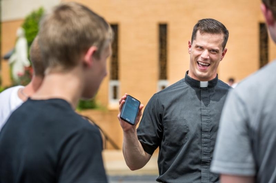 Father David Miloscia of Assumption Parish in St. Louis shows young people the game Pokemon Go on his cellphone as they chase Pokemon stops around the church grounds July 14. CNS photo/Lisa Johnston, St. Louis Review