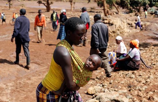 A woman carries her child near destroyed houses in Solai, Kenya