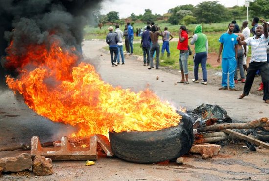 Protesters stand behind a burning barricade during protests over steep fuel price hikes Jan. 15 in Harare, Zimbabwe.