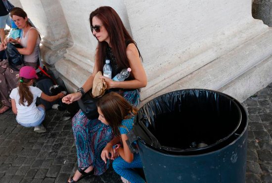 A woman holds water bottles next to a trash can under the St. Peter's Square colonnade at the Vatican
