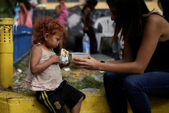 A volunteer with "Make the Difference" charity initiative gives a cup of soup and an "arepa" to a homeless child along a street in Caracas