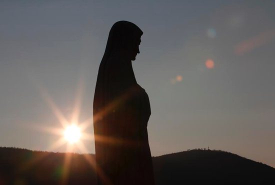 The sun sets behind a statue of Mary on Apparition Hill in Medjugorje, Bosnia-Herzegovina