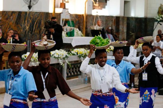 Women carry baskets of food on their heads as they dance