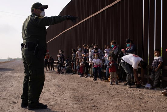 A Border Patrol agent in Penitas, Texas, instructs asylum-seeking migrants March 17, 2021, as they line up along the border wall after crossing the Rio Grande. Immigration and Customs Enforcement reports more than 12,000 coronavirus cases in detention centers.