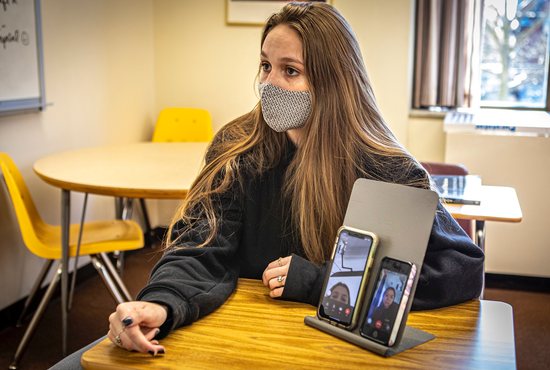 Catholic high school student Chelsea Venters sits next to a stand holding smartphones with two fellow students joining the class through FaceTime at Padua Academy in Wilmington, Del., March 30, 2021. The students participating virtually from home could participate in this particular lesson through smartphone technology.