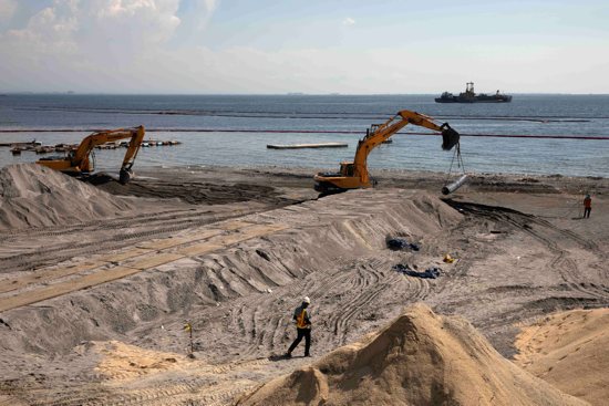 A worker stands on artificial sand or crushed dolomite, dumped on a portion of Manila Bay Sept. 4, 2020, as part of the Philippine government's efforts to rehabilitate and beautify the coastline. Two Philippine bishops are raising the alarm about rising sea levels that make the Philippine capital one of the fastest-sinking cities in the world.