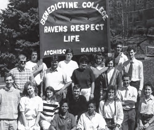 A 1990 yearbook photo of the pro-life group founded by Bishop Cozzens and his friends includes Father Joseph Taphorn (far left) and Bishop Andrew Cozzens (bottom row, second from right). The man on the far right with the tie (just above Bishop Cozzens) is now Father Alphonsus Hermes. The man whose head covers the “n” in Atchison is now Father Joseph Tatro.
