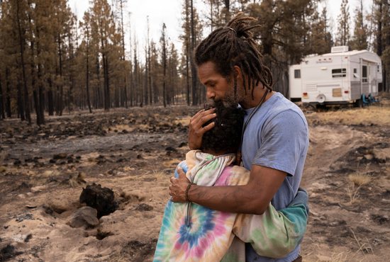 Nicolas Bey, 11, hugs his father, Sayyid Bey, within sight of a donated trailer they were using near Beatty, Ore., July 19, 2021, after their home was burned in the Bootleg Fire.