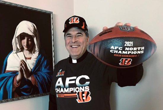 Father Tom Wray, Catholic chaplain of the Cincinnati Bengals, poses for a photo with the 2021 AFC North Champions ball Feb. 8, 2022. As part of his chaplaincy, Father Wray has conversations and provides spiritual guidance to those who work for the Bengals franchise.