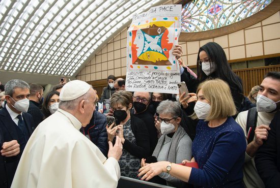 Pope Francis greets people near a banner in Italian calling for the pope's intervention with Russia, Ukraine and NATO, during his general audience in the Paul VI hall at the Vatican Jan. 19, 2022.