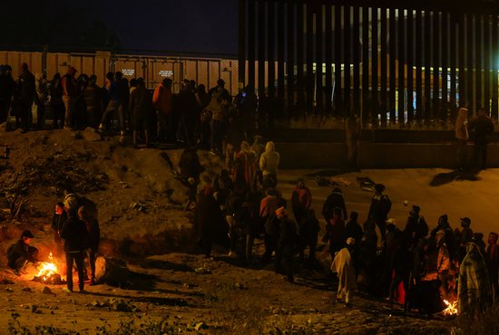 Migrants stand near the border wall after crossing the Rio Grande to turn themselves in to U.S. Border Patrol agents to request asylum in El Paso, Texas, Dec. 19, 2022. This photo is a view from Ciudad Juárez, Mexico.