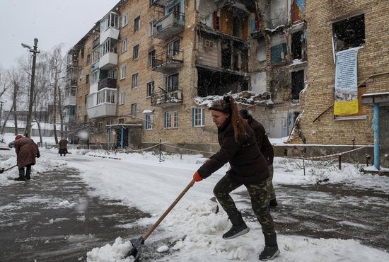 Local resident Tetiana Reznychenko shovels snow near her destroyed building, which has no electricity, heating and water, in Horenka, Ukraine, Nov. 19, 2022.