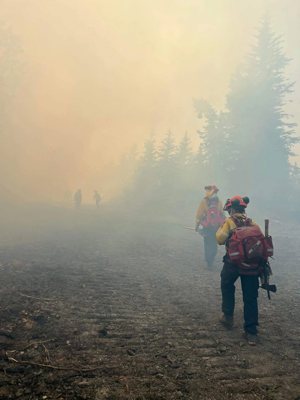 Firefighters are seen in an undated photo walking through smoke from wildfires in the Kimiwan Complex Fire SWF068 north of High Prairie, Alberta. Wildfires have always occurred, but experts say the warming climate is increasing their severity.