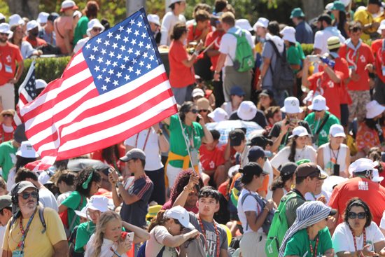 A U.S. pilgrim waves the American flag as he waits for the arrival of Pope Francis for the welcome ceremony for Pope Francis during World Youth Day at Eduardo VII Park in Lisbon, Portugal, Aug. 3, 2023.