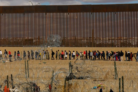 Migrants seeking asylum in the United States gather near the border wall Jan. 22, 2024, as seen from Ciudad Juarez, Mexico, after they crossed a razor wire fence and as members of the Texas National Guard stand guard.