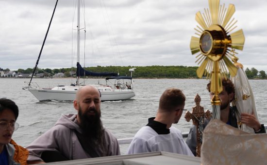 A man waves from a sailboat as the Eucharist travels by boat from New Haven to Bridgeport, Conn., May 19, 2024, as part of the National Eucharistic Pilgrimage.