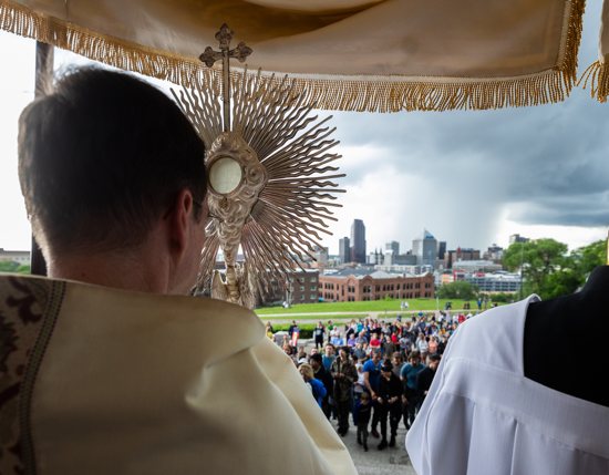 On the steps of the Cathedral of St. Paul in St. Paul, Father John Ubel, rector of the Cathedral, holds the Eucharist in a monstrance as those participating in the procession prepare to go inside for the final Benediction.
