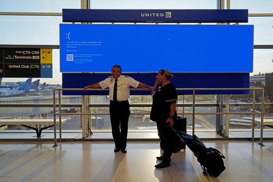 United Airlines employees wait by a departures monitor displaying a blue error screen, also known as the "Blue Screen of Death," inside Terminal C in Newark International Airport in New Jersey July 19, 2024, after United Airlines and other airlines grounded flights due to a worldwide tech outage caused by an update to CrowdStrike's "Falcon Sensor" software that crashed Microsoft Windows systems around the world. 