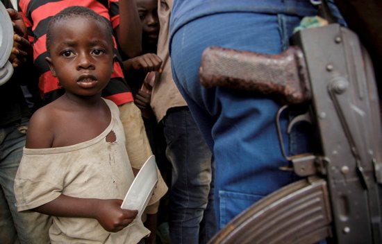 A child stands next to a police officer as displaced families wait for food at Rugombo Stadium in Burundi Feb. 18, 2025, after Congolese fled from renewed clashes between M23 rebels and the armed forces of the Democratic Republic of the Congo (FARDC). 