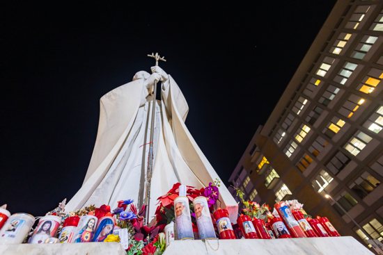 Votive candles and flowers are seen at the base of a statue of St. John Paul II outside Rome's Gemelli hospital Feb. 21, 2025, where Pope Francis is being treated for double pneumonia.