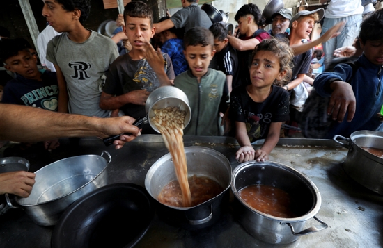 Young Palestinians displaced by the Israeli military offensive react May 21, 2025, while waiting to receive food cooked by a charity kitchen in Gaza City, Gaza Strip.