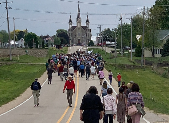 Pilgrims walk along a road toward Sts. Peter and Paul Catholic Church in Petersburg, Iowa, May 24, 2024. Pilgrimage organizers are encouraging Catholics to turn out in strong numbers for the National Eucharistic Pilgrimage's Eucharistic processions to counter the growing number of anti-Catholic protesters who consistently have been present at the route's public events.