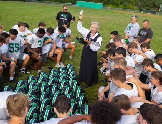 Benedictine Sister Linda Soler sprinkles holy water on Hill-Murray football players and their helmets at the end of practice Aug. 26. It is an annual ritual she initiated when she became chaplain of the football team.