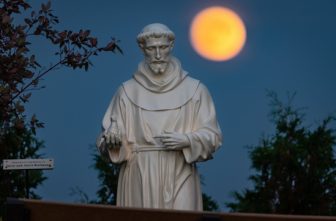 A hunter's moon rises behind a statue of St. Francis of Assisi on the grounds of the National Shrine of Our Lady of Champion in Champion, Wis., Oct 8, 2022.