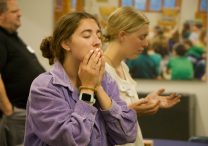 At left, Ellie Shaw, coordinator of middle school youth ministry at St. John the Baptist in New Brighton, prays during a praise and worship session at a Youth Discipleship and Faith Formation orientation Aug. 18-19 in St. Joseph Hall at the Archdiocesan Catholic Center (ACC) in St. Paul.