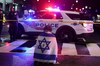 A man, with an Israeli flag with a cross in the center, kneels next to emergency personnel early May 22, 2025, as they work at the site where, according to the U.S. Department of Homeland Security, two Israeli Embassy staff were shot dead near the Capital Jewish Museum in Washington late May 21. The American Jewish Committee was hosting an evening event at the museum.
