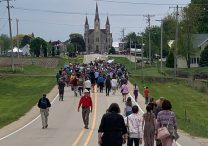Pilgrims walk along a road toward Sts. Peter and Paul Catholic Church in Petersburg, Iowa, May 24, 2024. Pilgrimage organizers are encouraging Catholics to turn out in strong numbers for the National Eucharistic Pilgrimage's Eucharistic processions to counter the growing number of anti-Catholic protesters who consistently have been present at the route's public events.