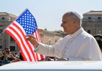 With a U.S. flag in the background, Pope Leo XIV waves to the crowd from the popemobile as he rides around St. Peter's Square at the Vatican before his weekly general audience Aug. 6, 2025.