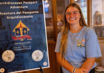 Susan Heselton stands by an Archdiocesan Passport Adventure sign at Nativity of Our Lord in St. Paul.  DAVE HRBACEK  |  THE CATHOLIC SPIRIT