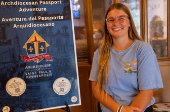 Susan Heselton stands by an Archdiocesan Passport Adventure sign at Nativity of Our Lord in St. Paul.  DAVE HRBACEK  |  THE CATHOLIC SPIRIT