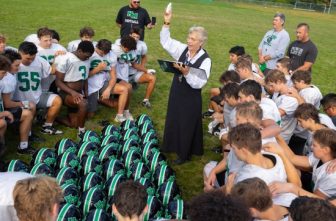 Benedictine Sister Linda Soler sprinkles holy water on Hill-Murray football players and their helmets at the end of practice Aug. 26. It is an annual ritual she initiated when she became chaplain of the football team.